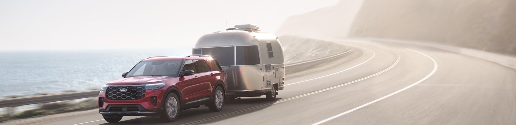 Ford SUV hauling camper along coastal highway
