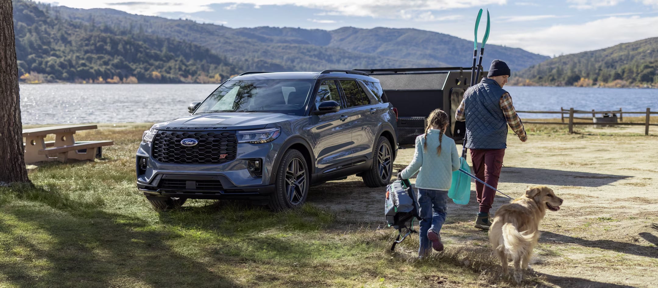 Family walking with their dog near a 2025 Ford Explorer parked by a scenic lake.