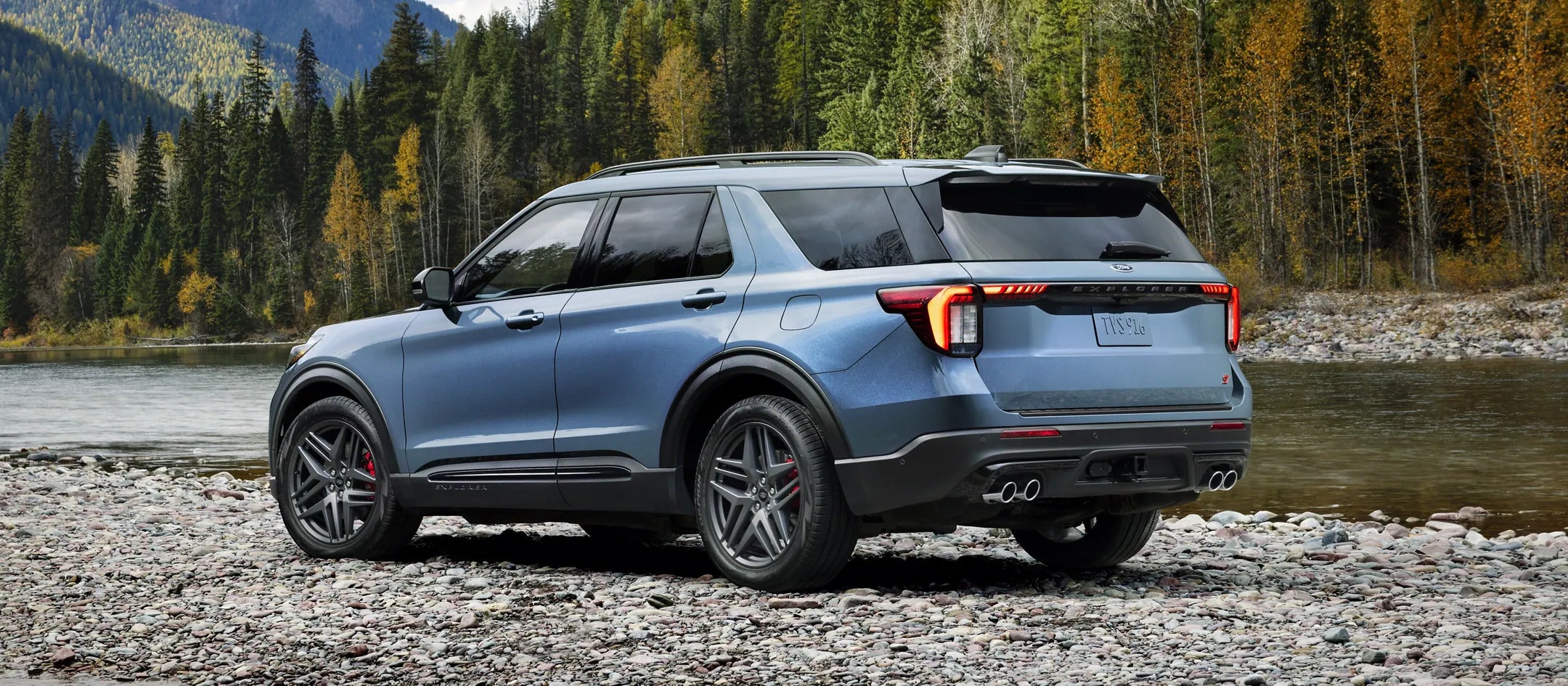2025 Ford Explorer rear view parked on a rocky terrain beside a river and surrounded by trees.